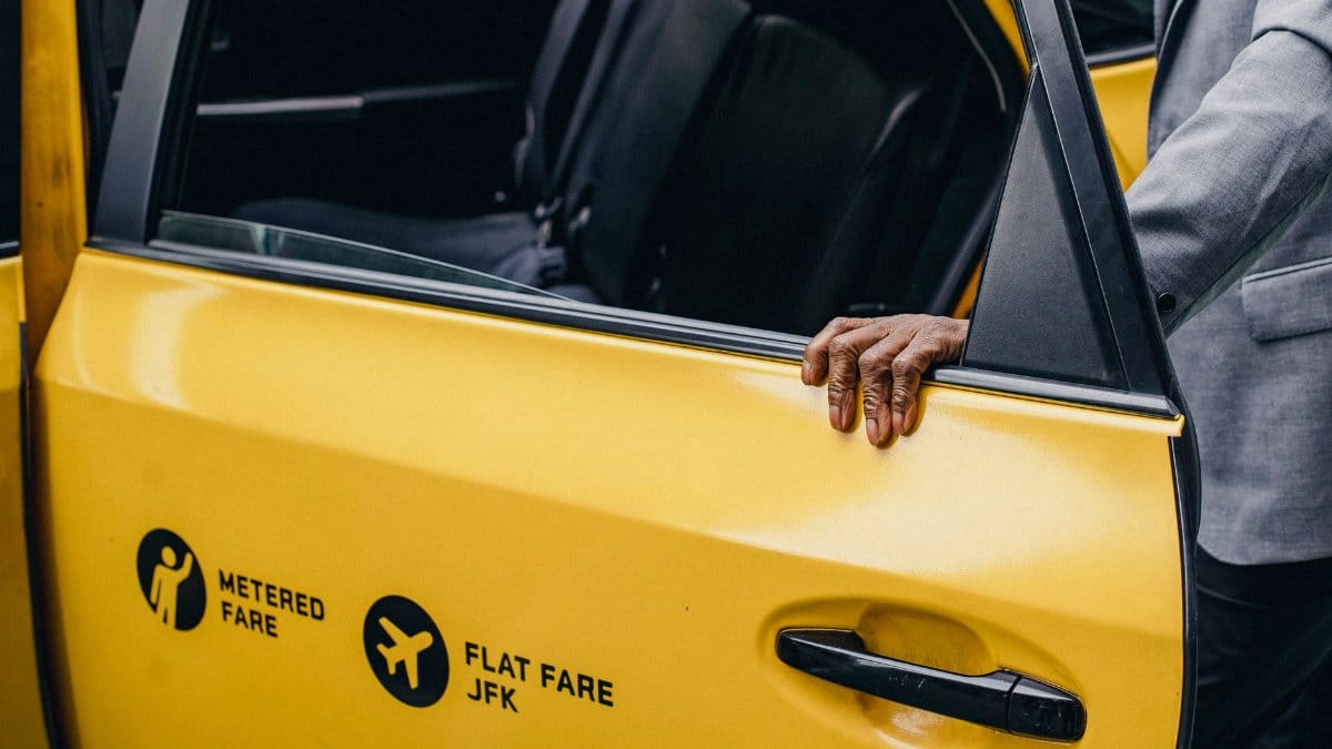 A person opens a yellow taxi door with JFK flat fare signage.