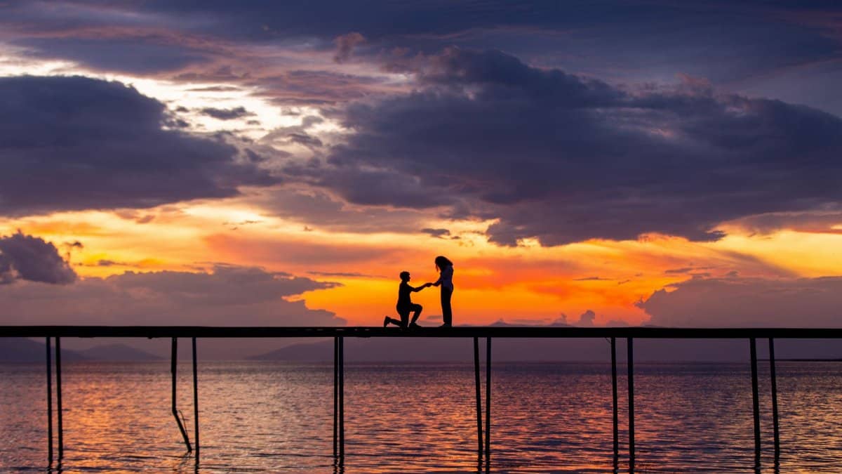 Silhouette of couple's proposal during sunset on a pier over ocean waters.