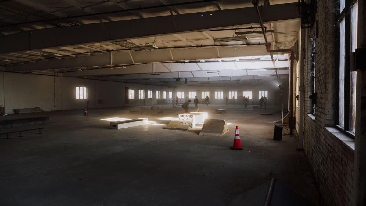 Empty indoor skate park with ramps and natural light streaming in, perfect for skating.