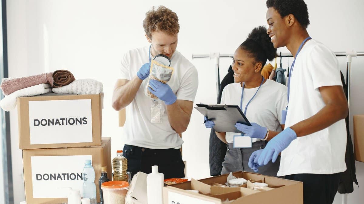 Three diverse volunteers sorting donation boxes filled with clothing and supplies indoors.