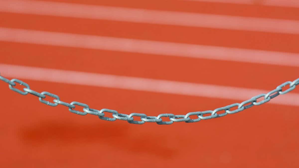 Detailed close-up of a metal chain against a vibrant red running track background.