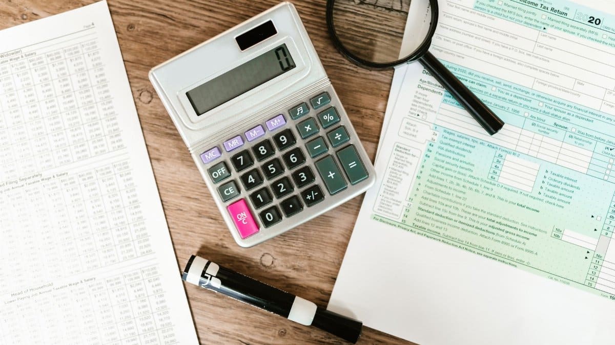 Top view of tax forms, a calculator, and a magnifying glass on a wooden surface, ideal for accounting themes.