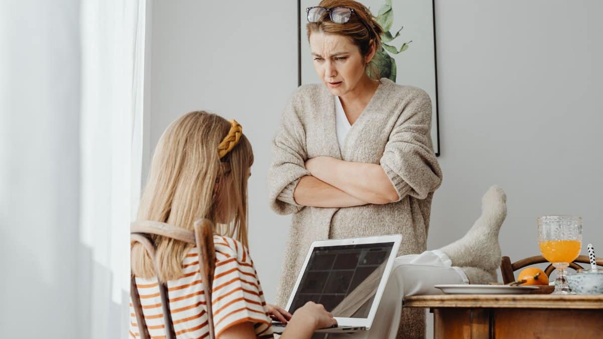 A mother talks seriously with her daughter sitting with a laptop in a cozy room.