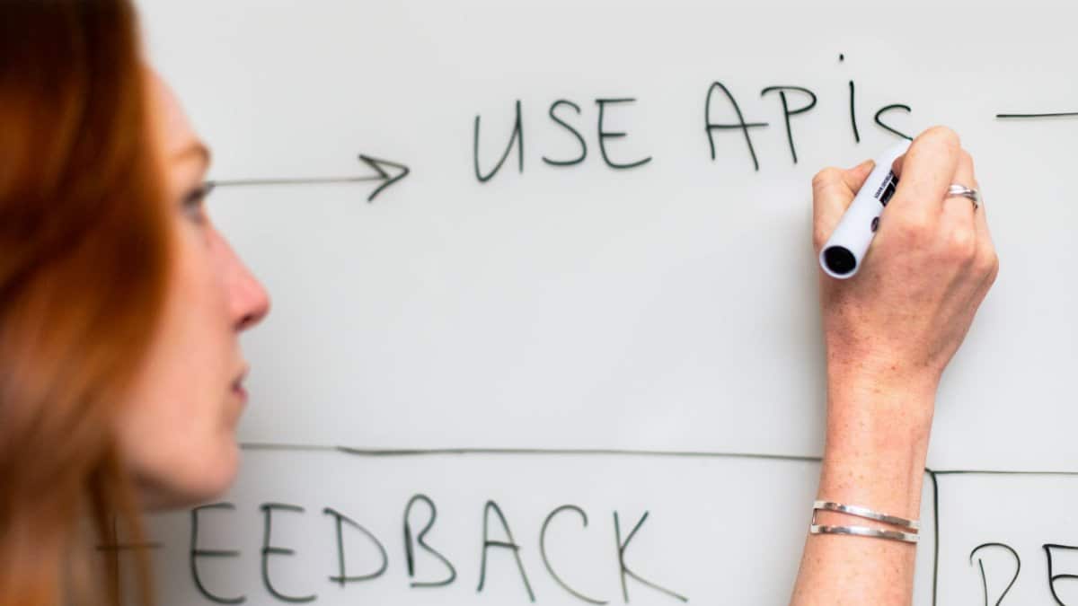 A woman writes 'Use APIs' on a whiteboard, focusing on software planning and strategy.