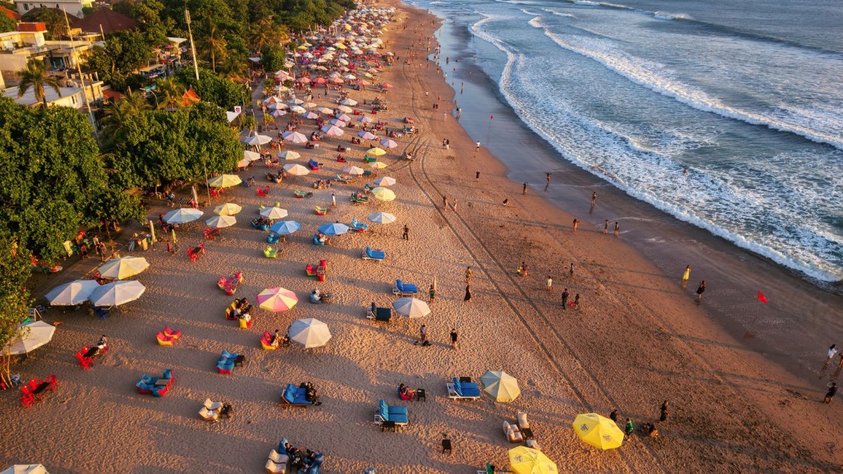 Aerial shot of lively beach with colorful umbrellas and ocean waves in Bali, Indonesia.