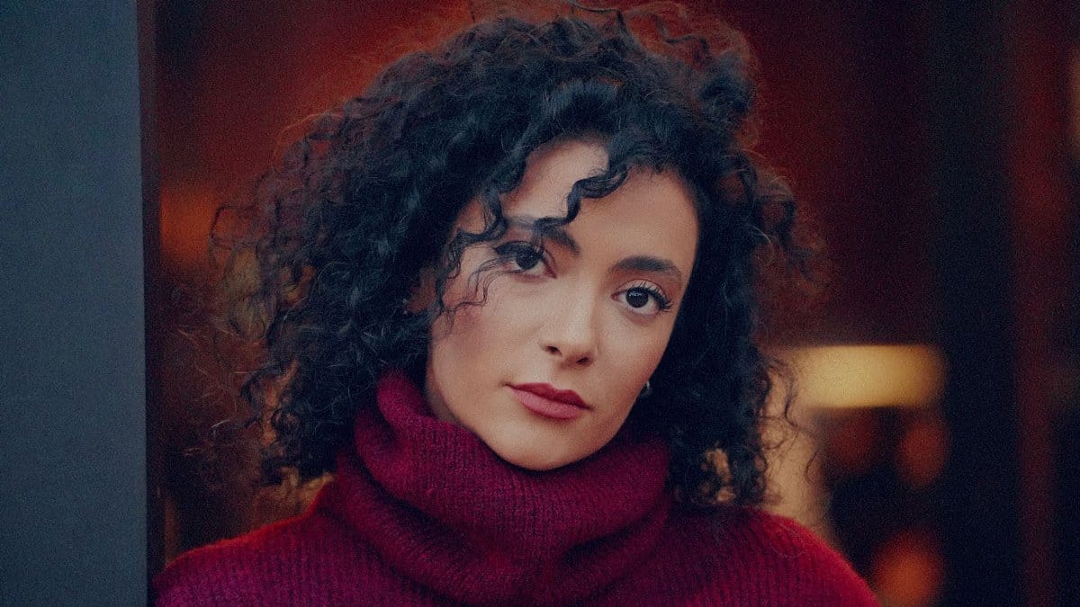A warm and intimate portrait of a woman with curly hair wearing a burgundy turtleneck sweater.