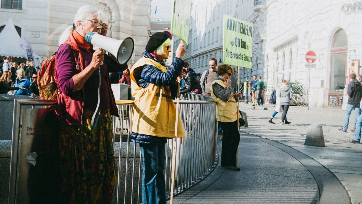 A vibrant protest scene in Vienna with diverse participants holding signs and a megaphone.