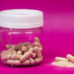 A glass jar filled with capsules on a vibrant pink background, showcasing health supplements.
