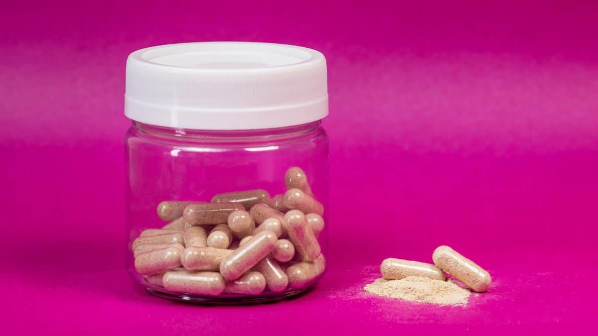 A glass jar filled with capsules on a vibrant pink background, showcasing health supplements.