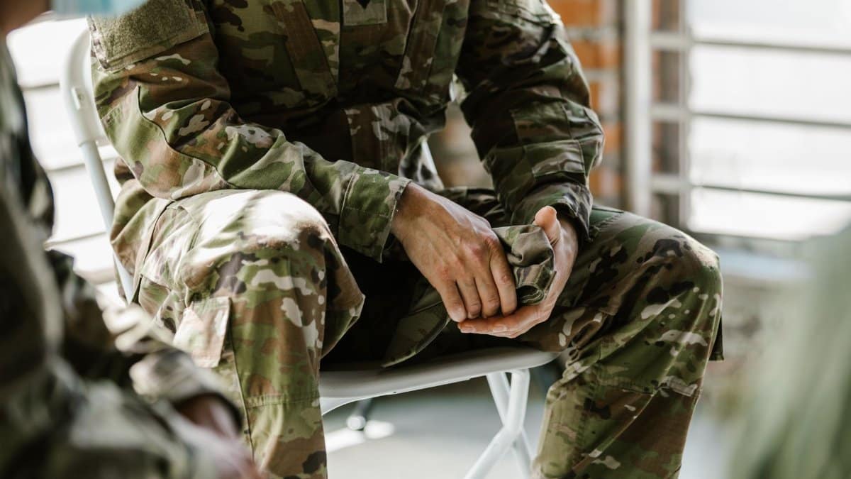 A soldier in camouflage uniform sitting indoors, representing military life and service.