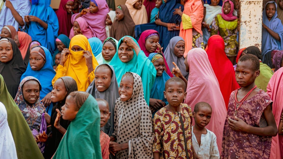 A joyful crowd gathers outdoors wearing colorful traditional attire.