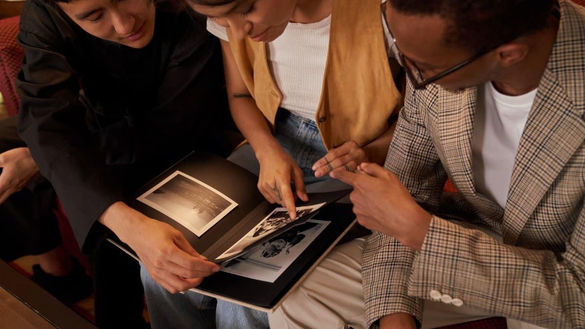 Three friends gather to share memories from a photo album, highlighting friendship and nostalgia.