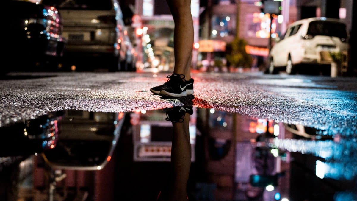 A vibrant urban city street at night, showcasing reflections in a puddle and bustling nightlife.