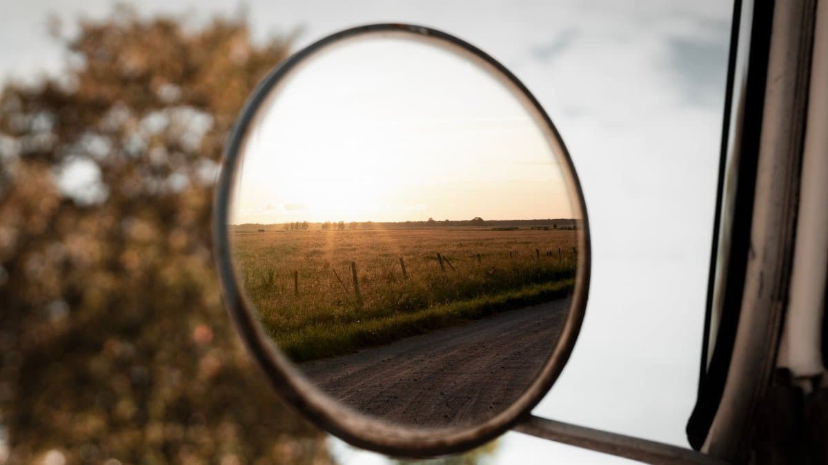 A serene countryside landscape reflected in a car's side mirror during sunset.