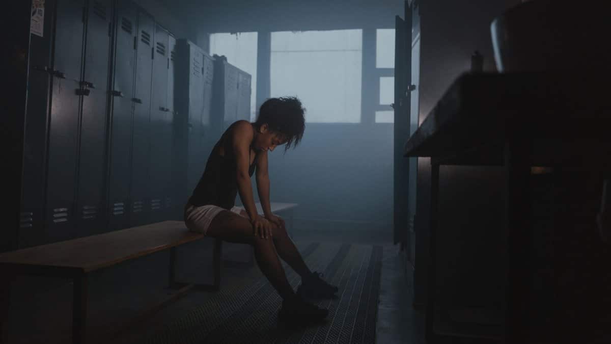 A tired athlete rests on a bench in a dim locker room, capturing a moment of reflection and exhaustion.