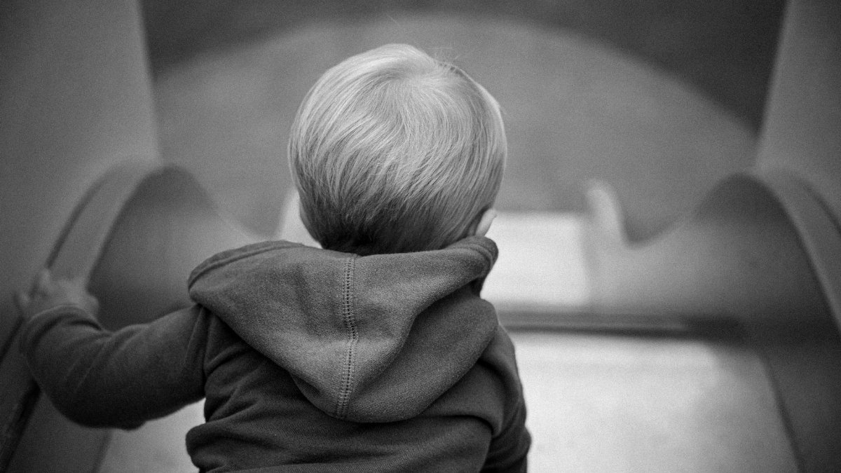 Black and white photo of a child crawling up a slide in an outdoor play area.