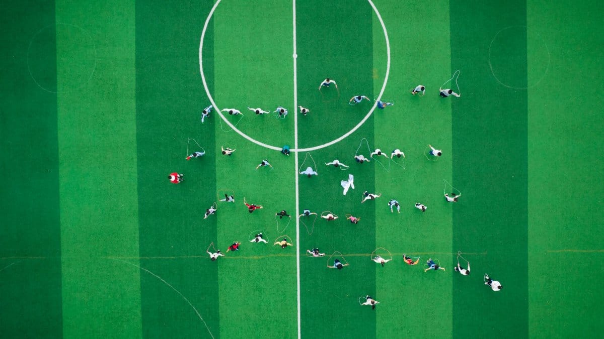 Top view of a group exercising with jump ropes on a vibrant green sports field.