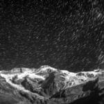 Long exposure of star trails over majestic snow-covered mountains at night.