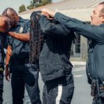 Law enforcement officers performing a pat-down on two individuals in an urban setting.
