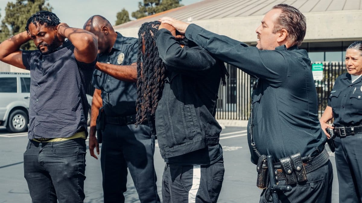 Law enforcement officers performing a pat-down on two individuals in an urban setting.