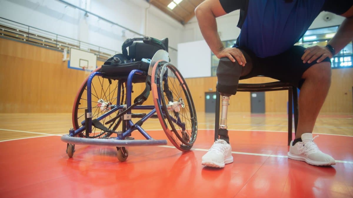 A focused shot of an adaptive athlete with a prosthetic leg taking a break on a basketball court indoors.