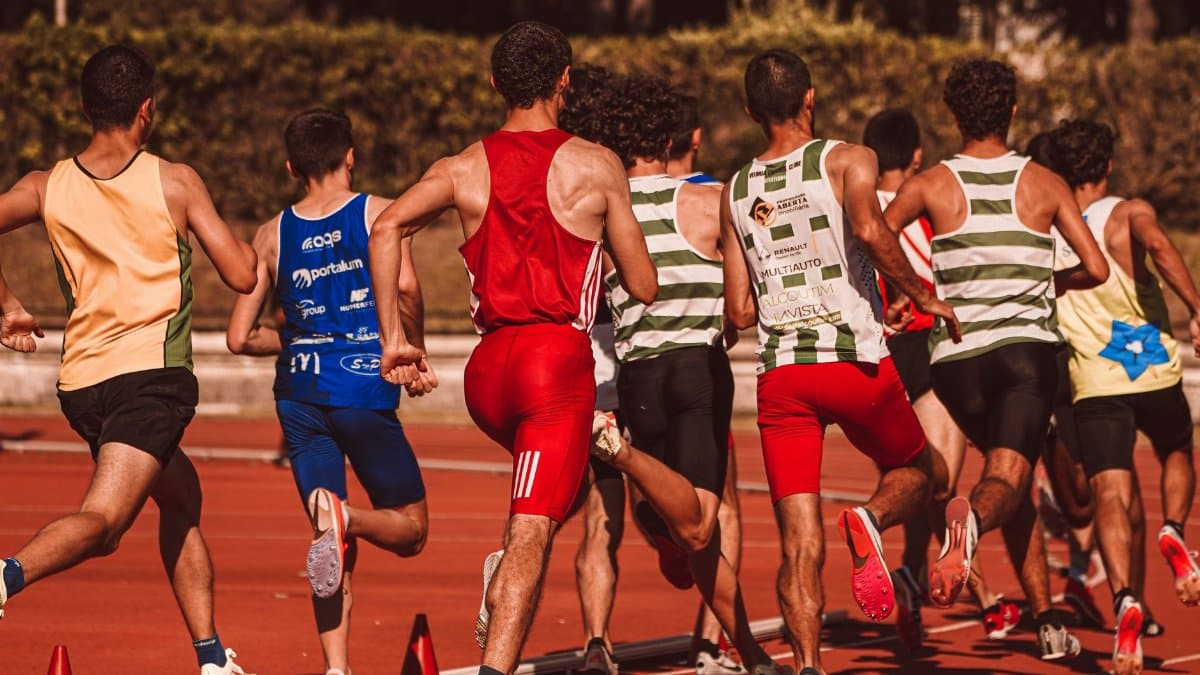 A group of male athletes competing in a track and field event outdoors under a sunny sky.