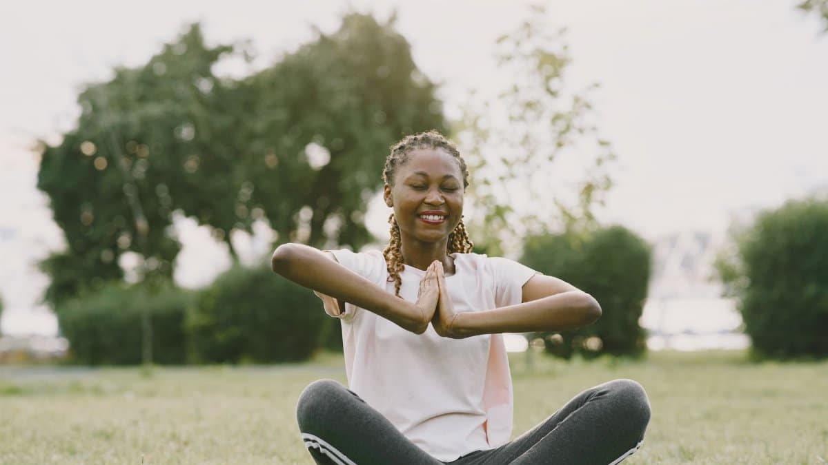 African American woman practicing yoga in a sunny park, enjoying relaxation and wellness outdoors.