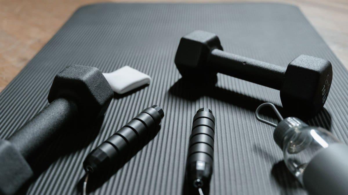 Close-up of dumbbells, jump rope, and water bottle on a yoga mat, ideal for home fitness routines.