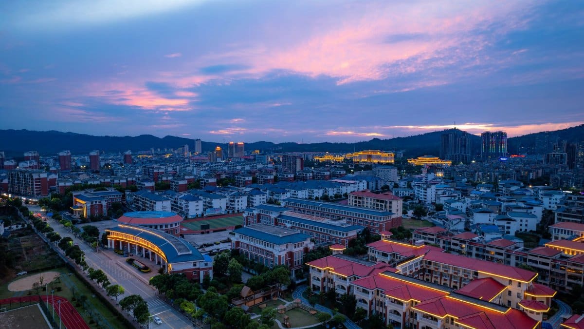 A stunning aerial view of Jiujiang City, China, at twilight with vibrant city lights and a colorful sunset sky.