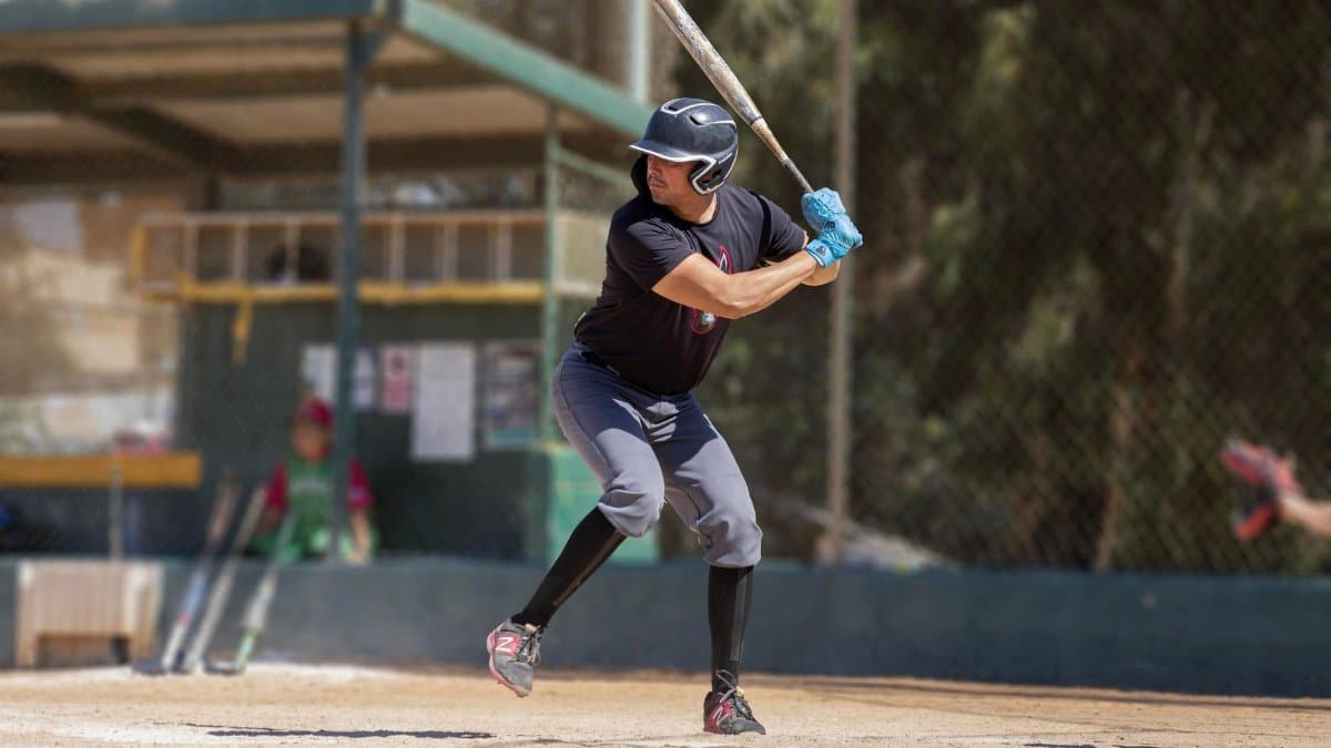 A baseball player in action at a sunlit outdoor baseball field, preparing to swing.