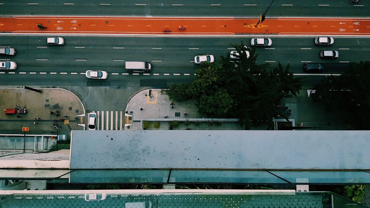 Aerial shot of an urban road with vehicles, bike lane, and pedestrians, captured from above.