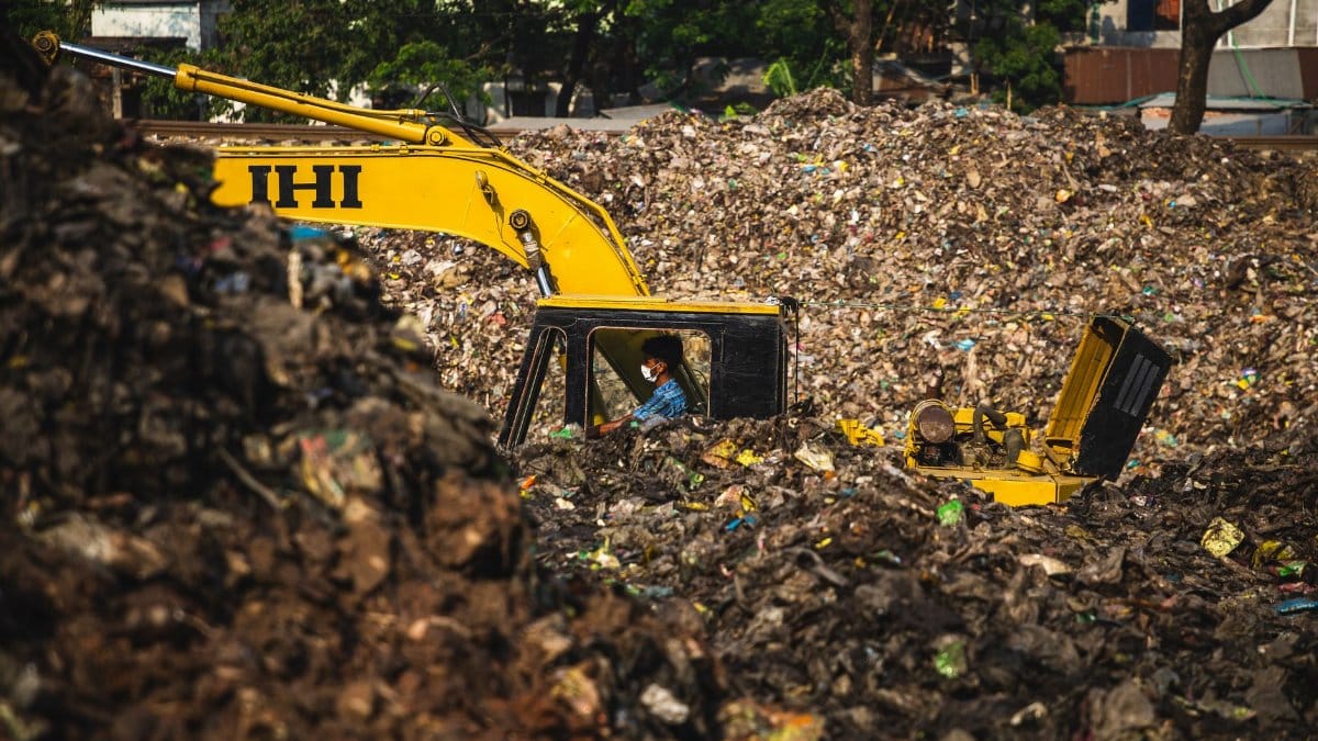 Excavator and worker managing waste at a landfill site, highlighting pollution issues.