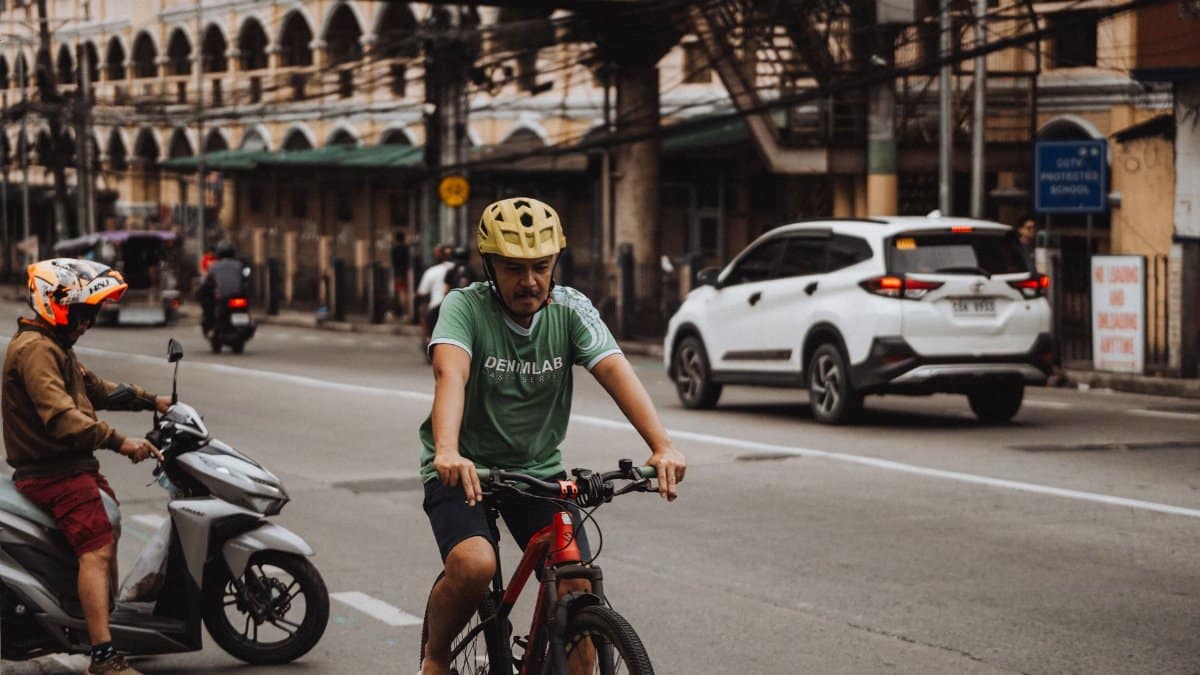 A cyclist wearing a helmet rides alongside city traffic in a bustling urban area street.