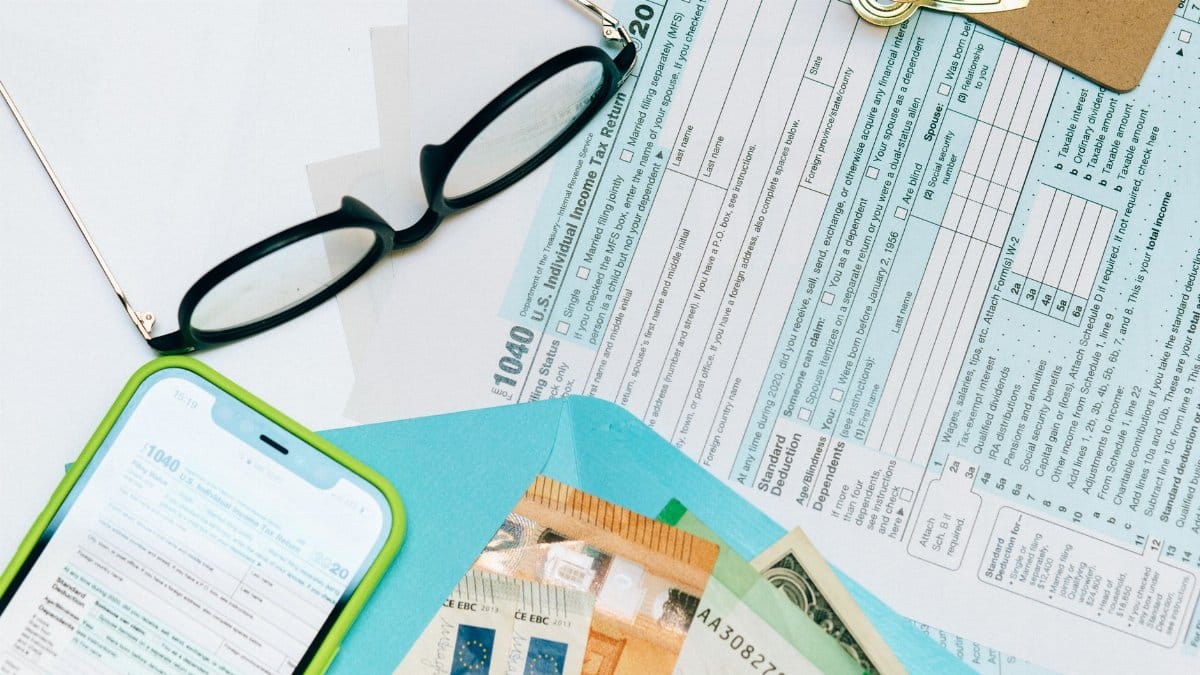 Close-up of tax forms, smartphone, and dollar bills for financial analysis and preparation.