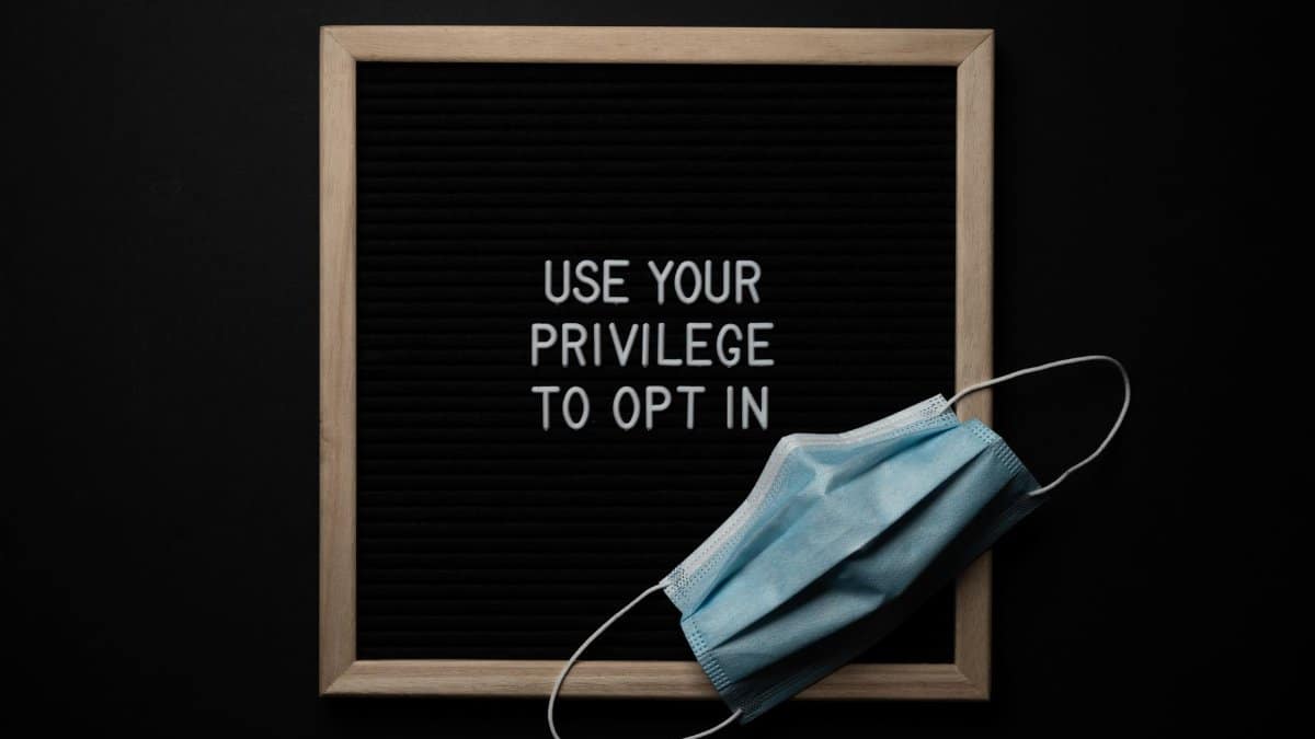 Top view of sterile mask on blackboard with Use Your Privilege To Opt In inscription on black background