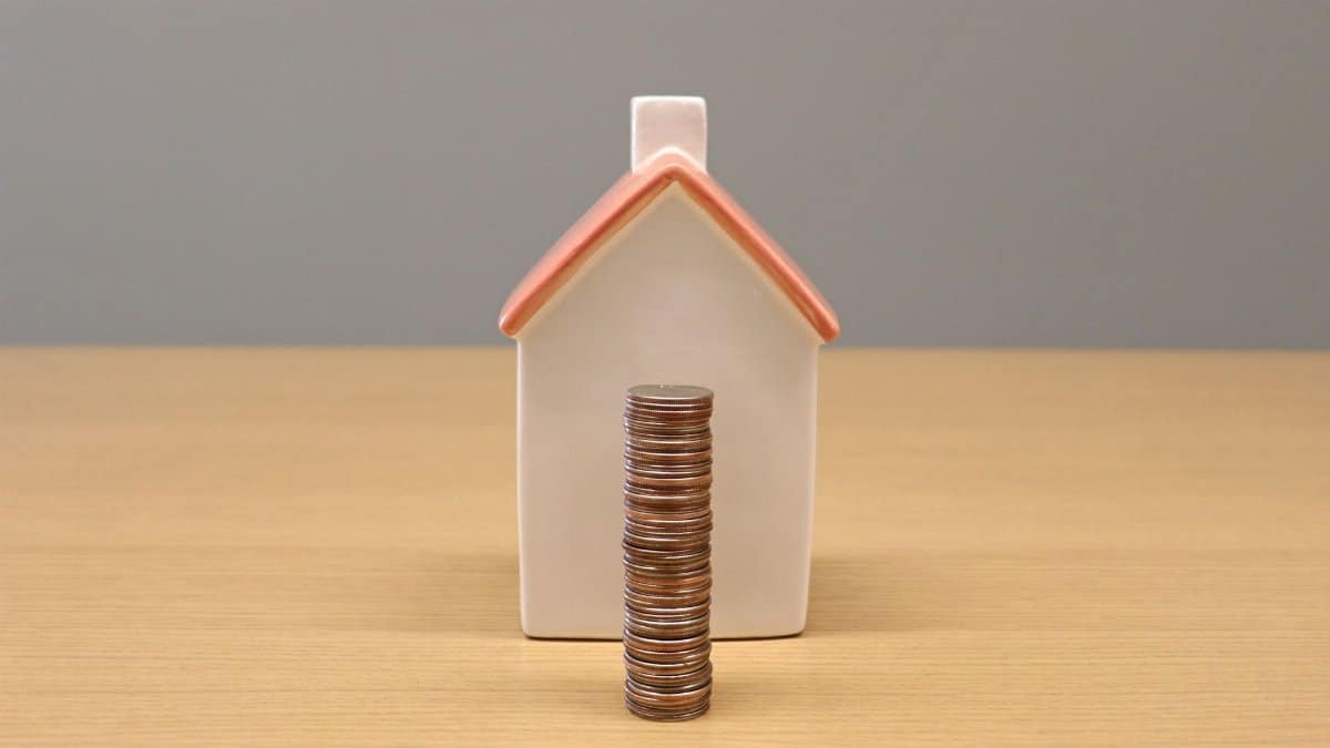 A conceptual still life image of stacked coins in front of a porcelain house, symbolizing savings and investment.