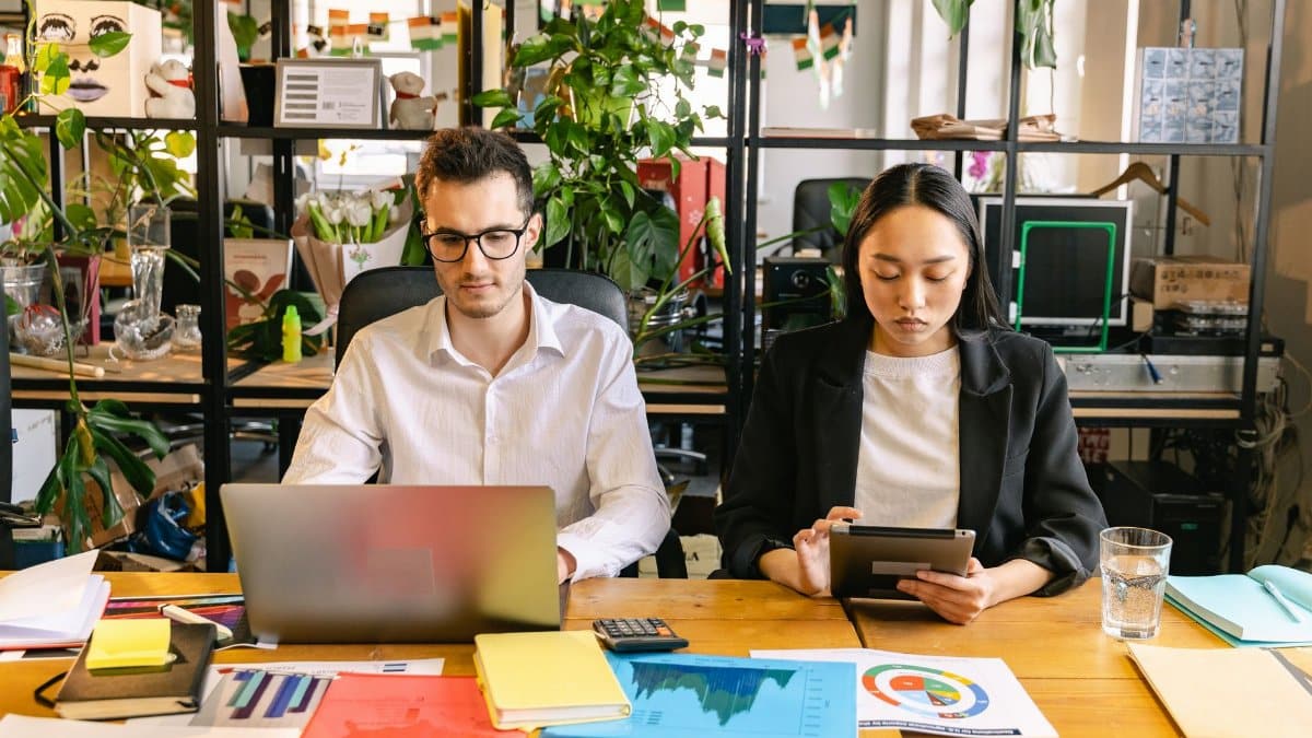 Two professionals working with laptops and tablets in a modern coworking space surrounded by plants.