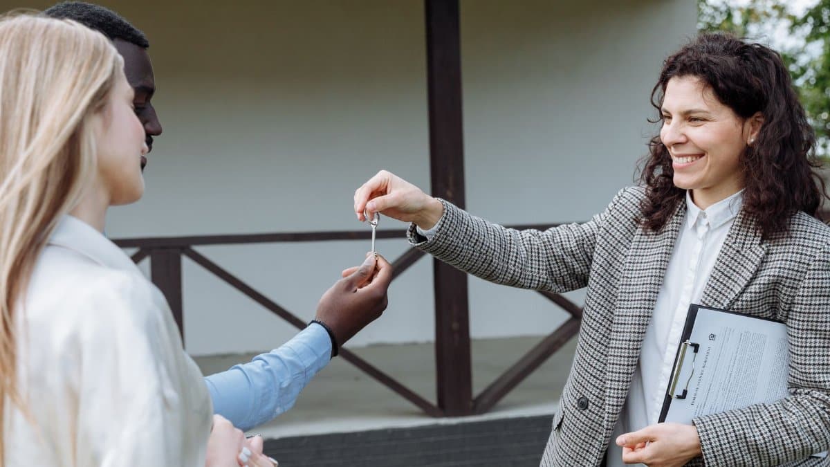 Real estate agent giving house keys to a happy couple outside their new home.