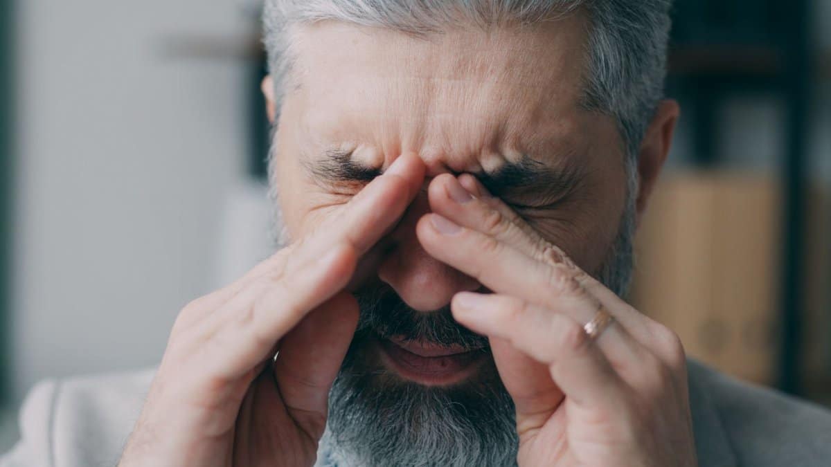 Close-up of a senior man rubbing his eyes experiencing stress indoors.