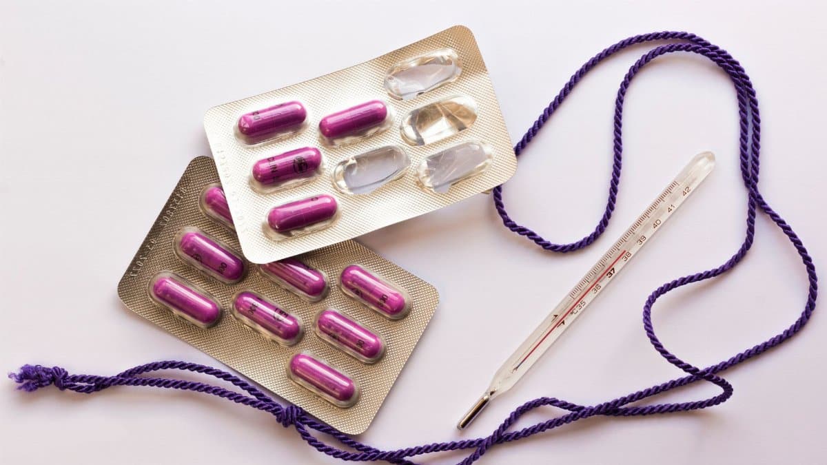 Image of pills and a thermometer on a white background, useful for healthcare themes.