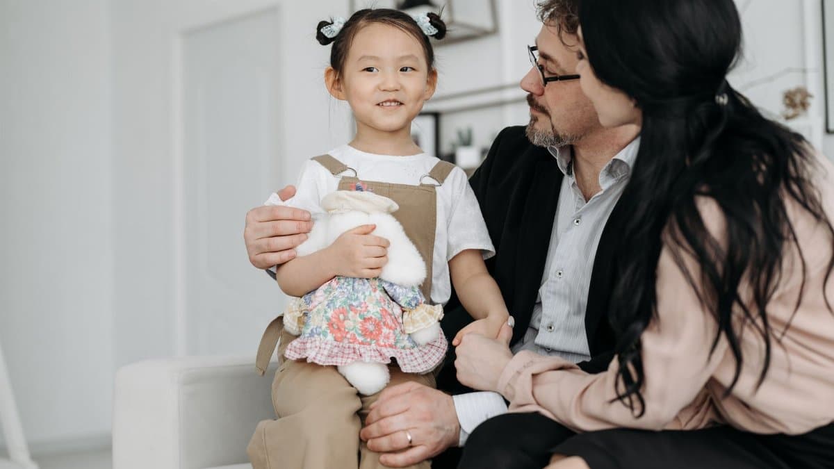 A joyful family scene with adopted child cuddling a stuffed toy indoor setting.