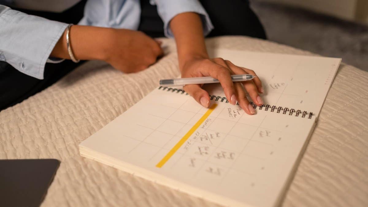 Close-up of a person scheduling in a spiral-bound planner using a pen. Indoor setting.