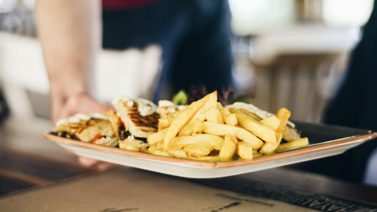 Close-up of delicious french fries and sandwich served on a plate indoors.
