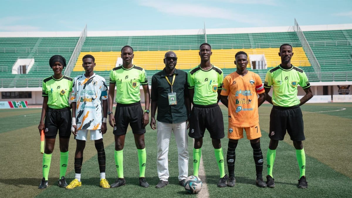 A soccer team with officials posing on a field during daytime at a stadium.