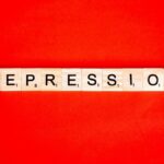 Word depression spelled with letter tiles on vibrant red background, highlighting mental health theme.
