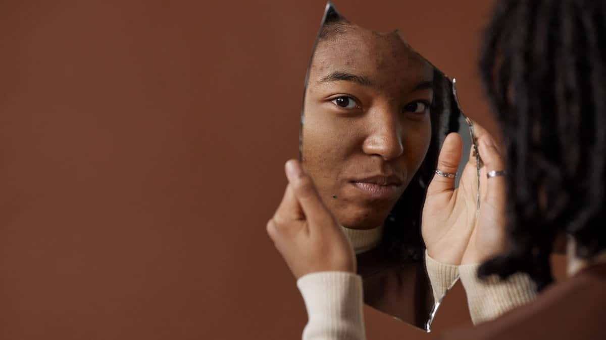 A woman holding and looking into a broken mirror, reflecting on self image and identity.