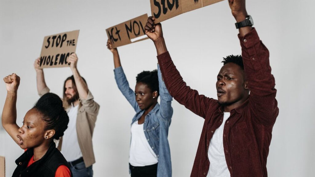 A diverse group of adults holding protest signs indoors, advocating against violence.
