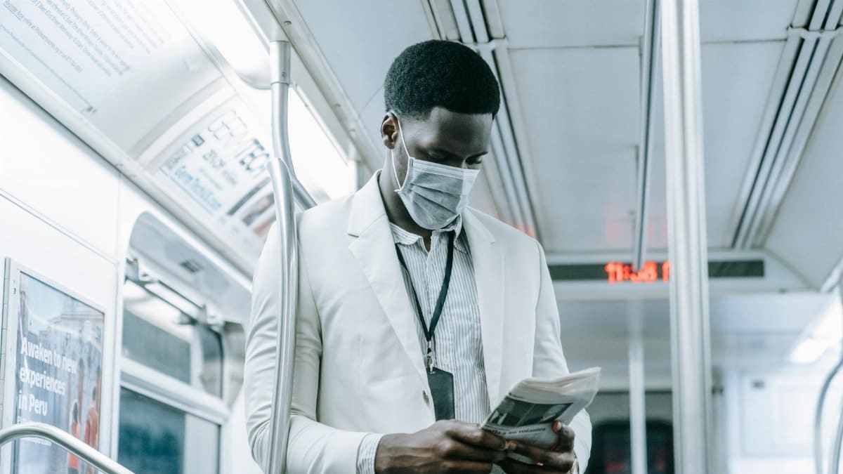 A man in a face mask reads a newspaper on public transportation during the pandemic.