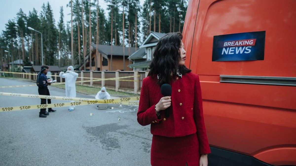 A reporter in red documents a crime scene with investigators in protective suits.