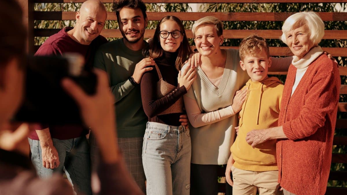 A joyful family portrait featuring multiple generations smiling outdoors in daylight.
